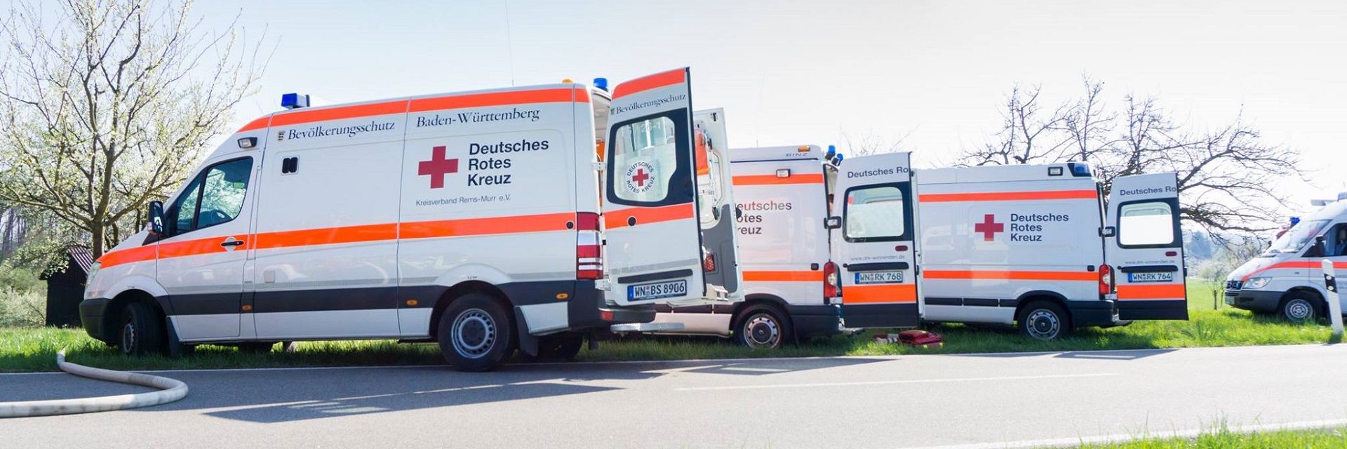 Foto: Eine junge Frau mit dunklen Locken blickt in die Kamera. Sie trägt eine Rotkreuzjacke und wirkt insgesamt sehr verantwortungsbewusst.